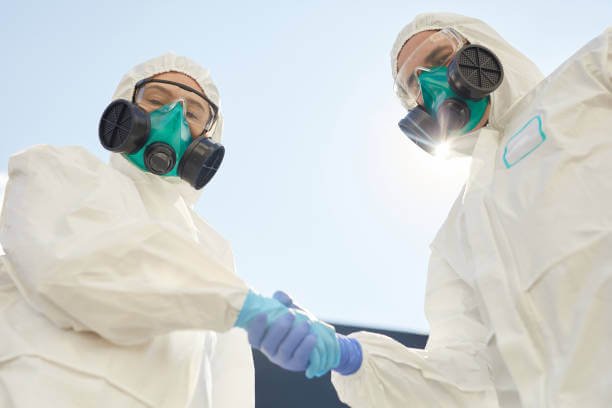 Low angle view at two workers wearing hazmat suits holding hands and looking at camera while standing against sky background, copy space