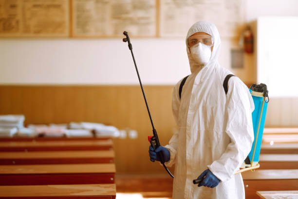 Portrait of man in protective hazmat suit with spray chemicals disinfecting school class. COVID-19.